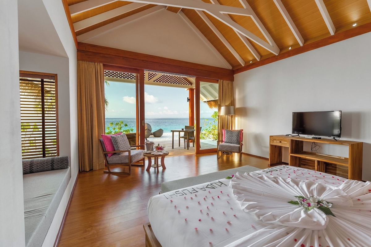 A bedroom with a bed, a TV, a desk, and a view of the ocean.