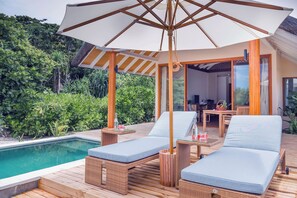 A poolside area with two lounge chairs, a table with a bottle and glass, and a large umbrella. - Kudafushi Resort & Spa (Kudafushi)