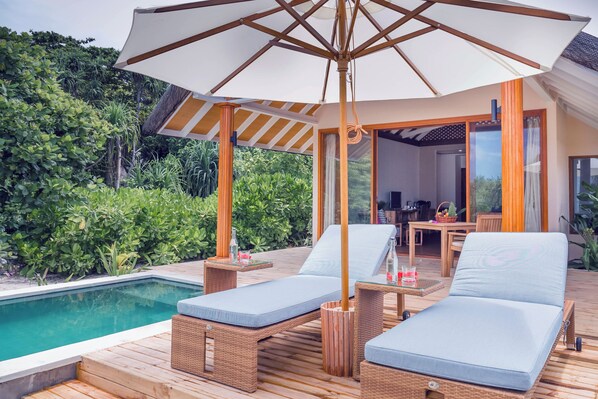 A poolside area with two lounge chairs, a table with a bottle and glass, and a large umbrella. - Kudafushi Resort & Spa (Kudafushi)