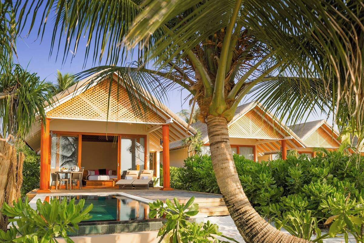 Un resort con dos cabañas de techo de paja, una piscina y exuberante vegetación tropical.