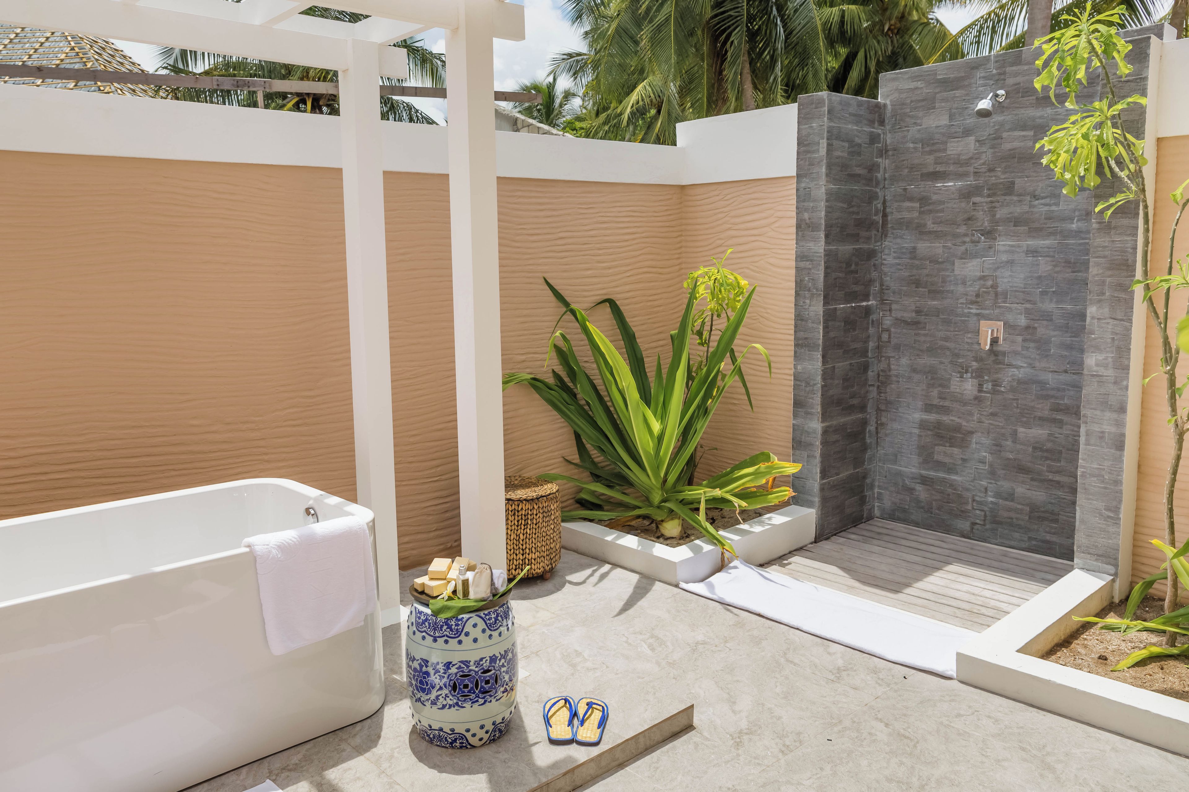 A modern outdoor bathroom with a bathtub, a shower, and a potted plant.