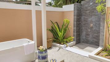 A modern outdoor bathroom with a bathtub, a shower, and a potted plant.