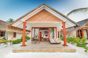 A beachfront villa with a thatched roof, wooden deck, and a covered outdoor seating area.