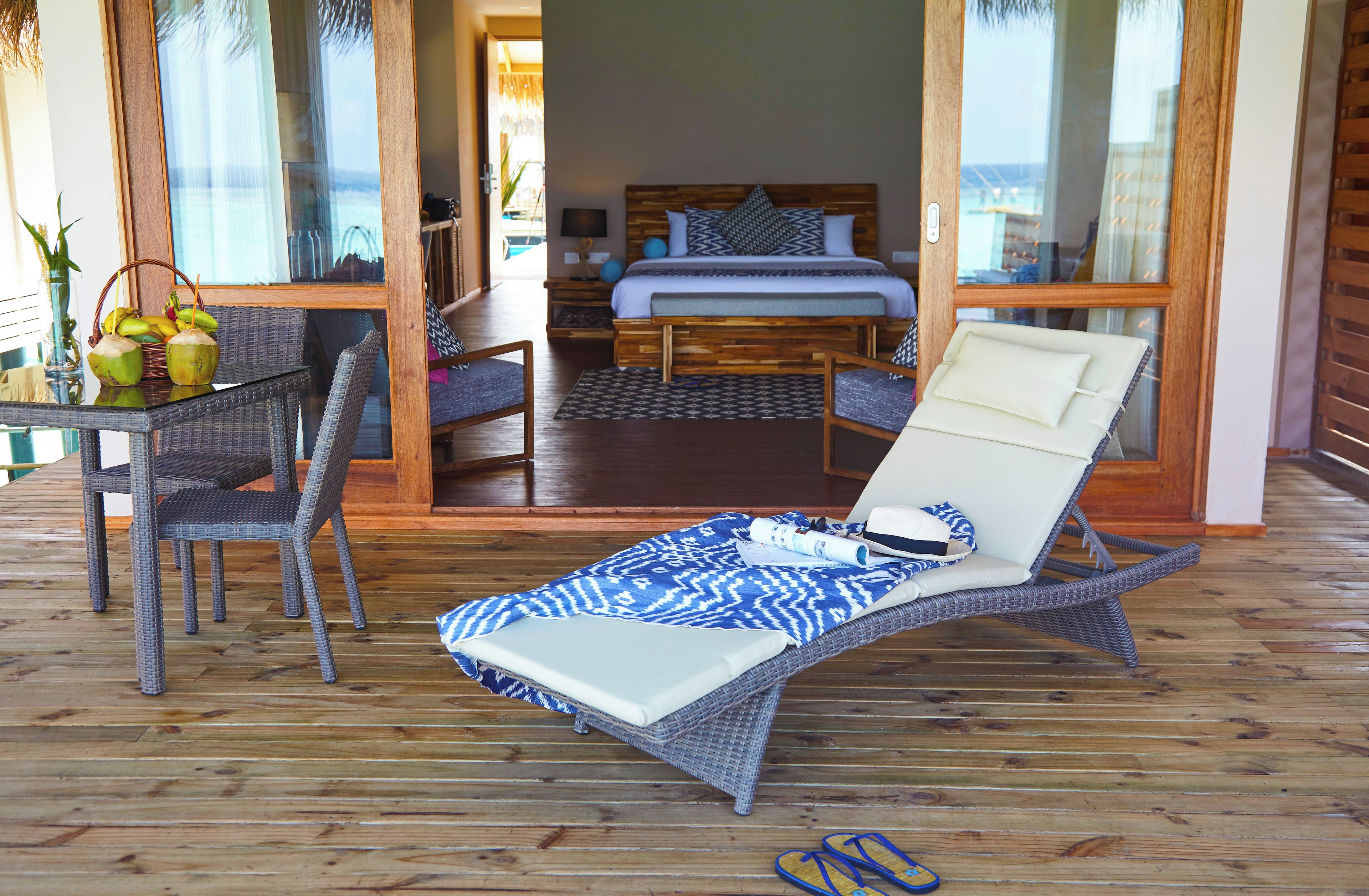 Una habitación con cama, un sillón, una mesa con cocos y vistas a través de un ventanal.