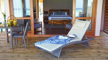 Una habitación con cama, un sillón, una mesa con cocos y vistas a través de un ventanal.