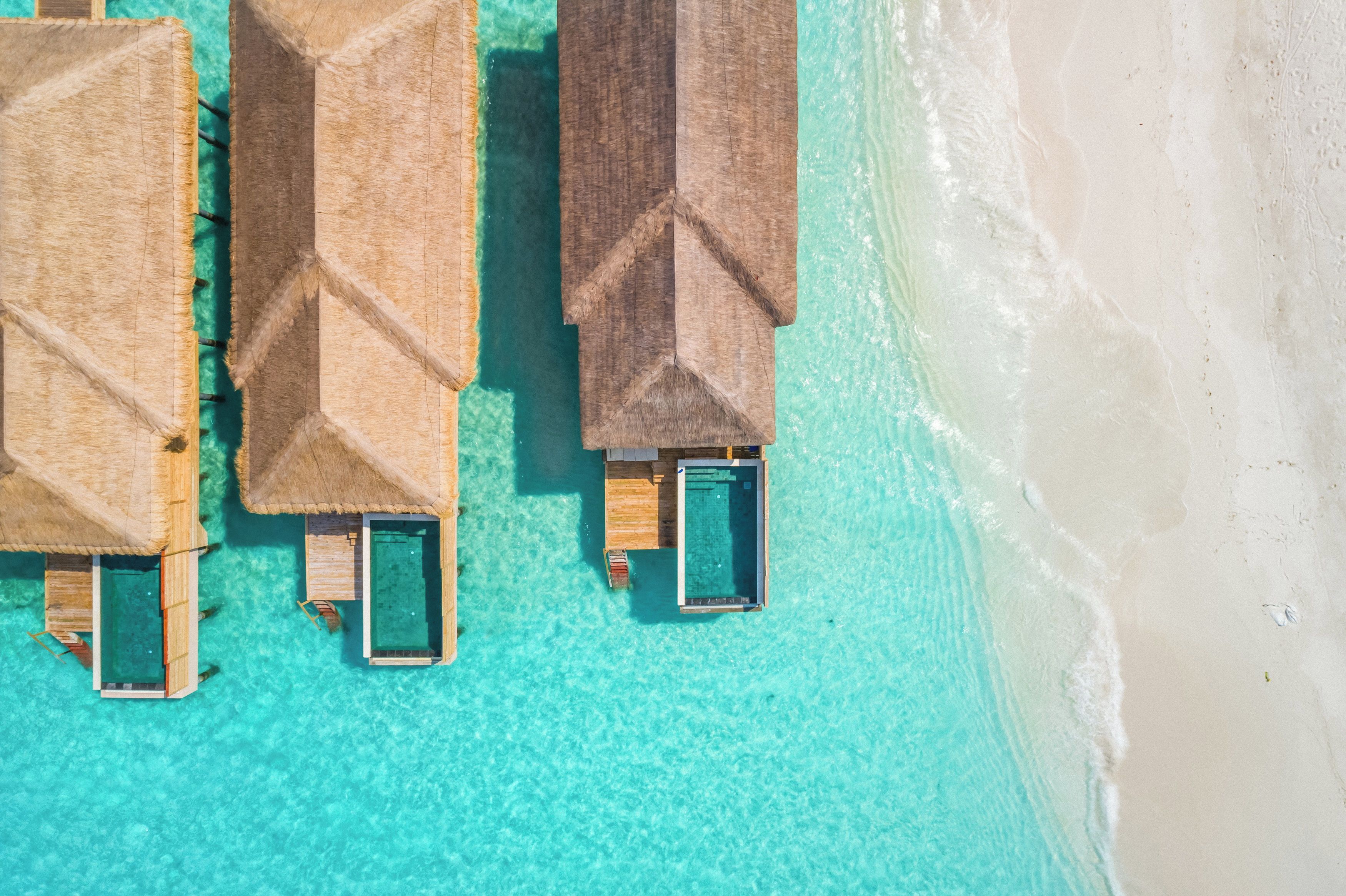 Overwater bungalows with private pools, connected by walkways, on a clear turquoise beach.