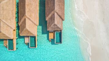 Overwater bungalows with private pools, connected by walkways, on a clear turquoise beach.