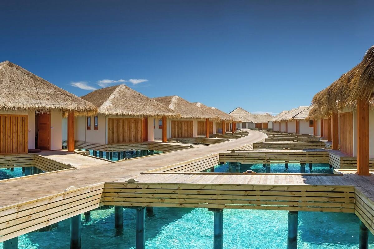 Bungalows sobre el agua con techos de paja y pasarelas de madera que llevan a piscinas infinitas.