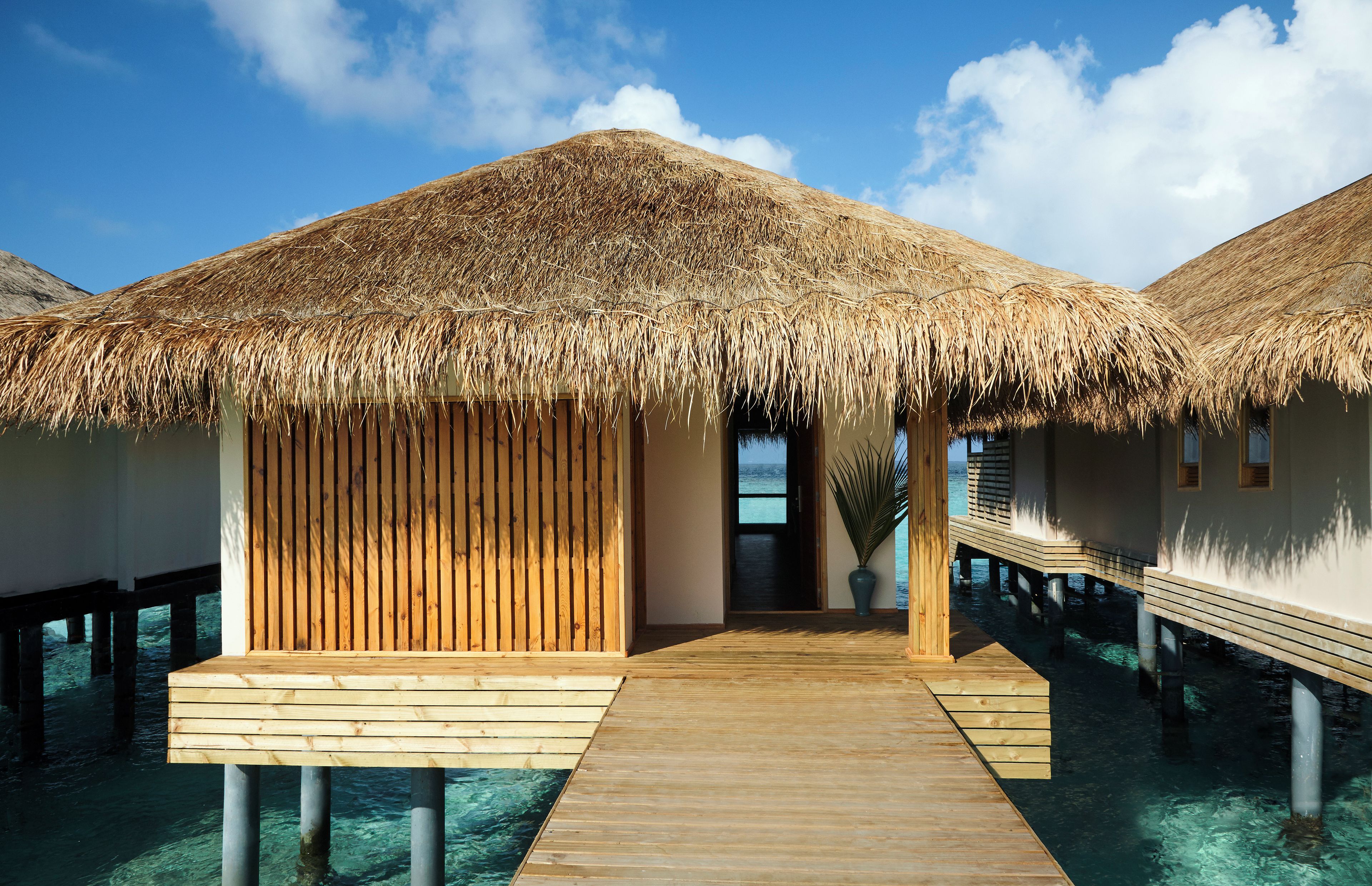 Overwater bungalows with thatched roofs, wooden walkways, and clear blue water.