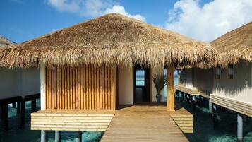 Overwater bungalows with thatched roofs, wooden walkways, and clear blue water.