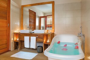 A bathroom with a wooden vanity, a large mirror, a bathtub with rose petals, and a shower. - Kudafushi Resort & Spa (Kudafushi)