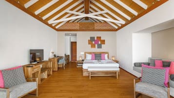A hotel room with a wooden ceiling, a bed with patterned pillows, a desk with a computer, and a TV.