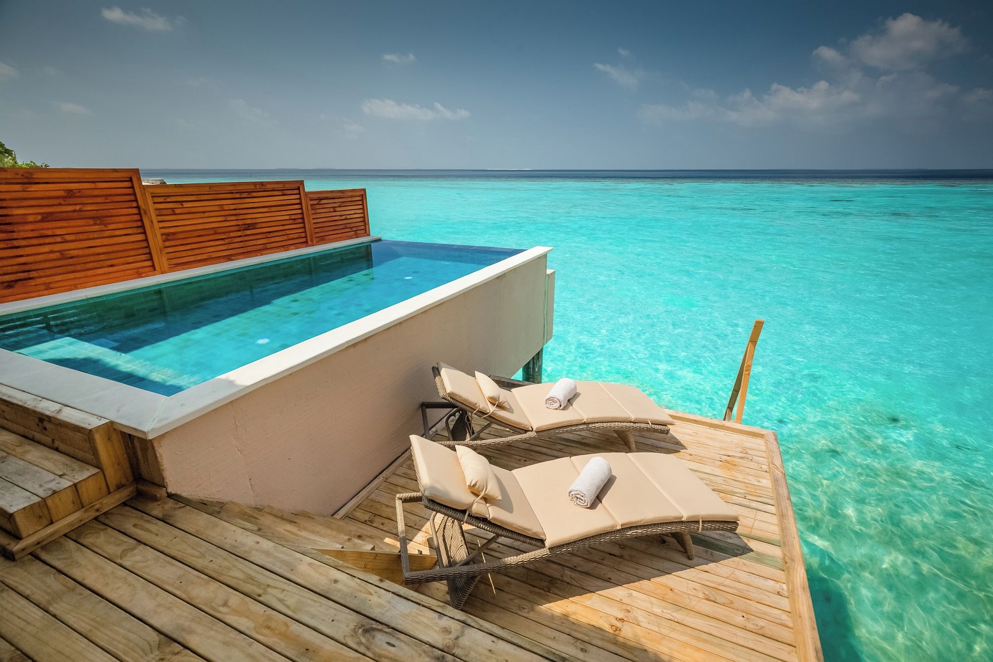A wooden deck with a pool and lounge chairs overlooking turquoise water.