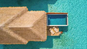 An aerial view of a resort with a clear blue pool, a thatched roof structure, and wooden lounge chairs.