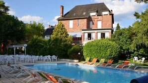 A swimming pool with lounge chairs, a brick house in the background, and a well-maintained garden.