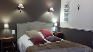 A bedroom with a bed, two bedside tables, two wall-mounted lamps, and a wall with a key holder and a calendar. - Logis Relais Du Quercy (Meyssac)
