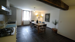 A kitchen with a gas stove, a sink, and cabinets. There is a dining table with chairs and a potted plant. - Logis Relais Du Quercy (Meyssac)
