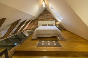 A bedroom with a sloped ceiling, a bed, a nightstand, a lamp, and a stone wall.