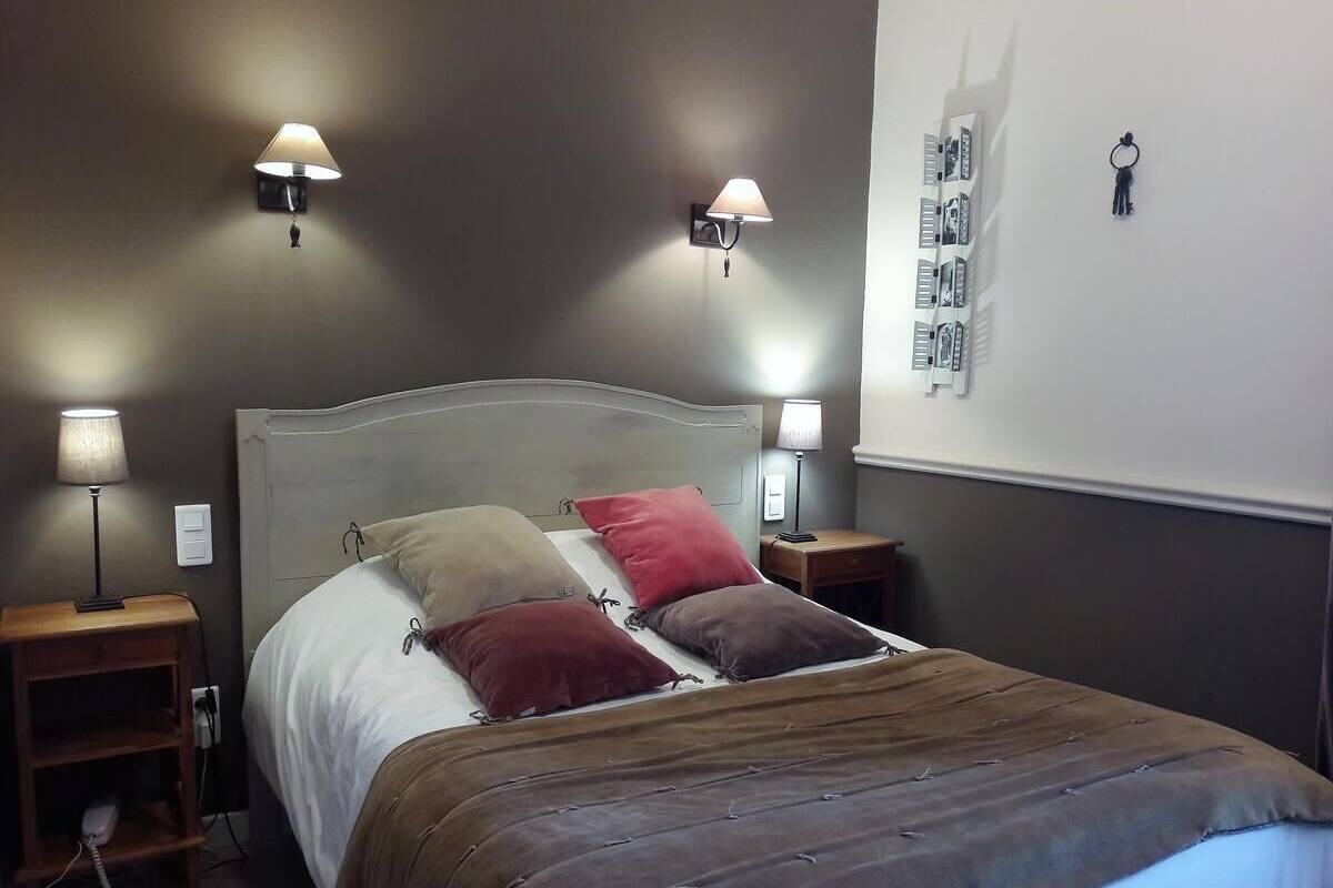 Un dormitorio con cama, dos mesitas de noche, dos lámparas de pared y una pared con un atril para llaves y un calendario.
