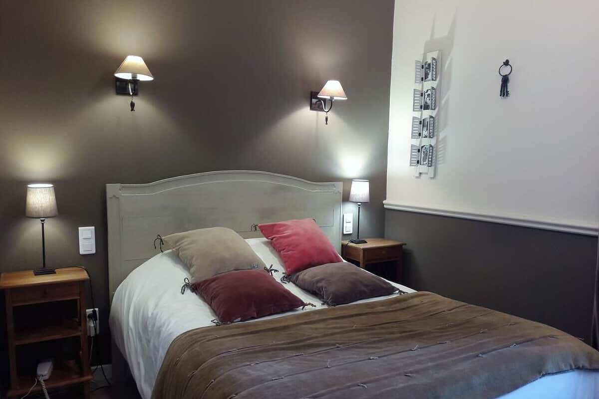 Quarto com cama, duas mesas de cabeceira, duas luminárias e um painel com porta-chaves e calendário.