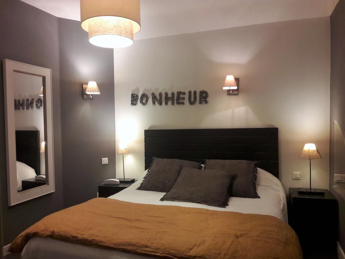 Un dormitorio con una cama, dos lámparas de noche, un espejo y un cartel en la pared que dice 'BONHEUR'.