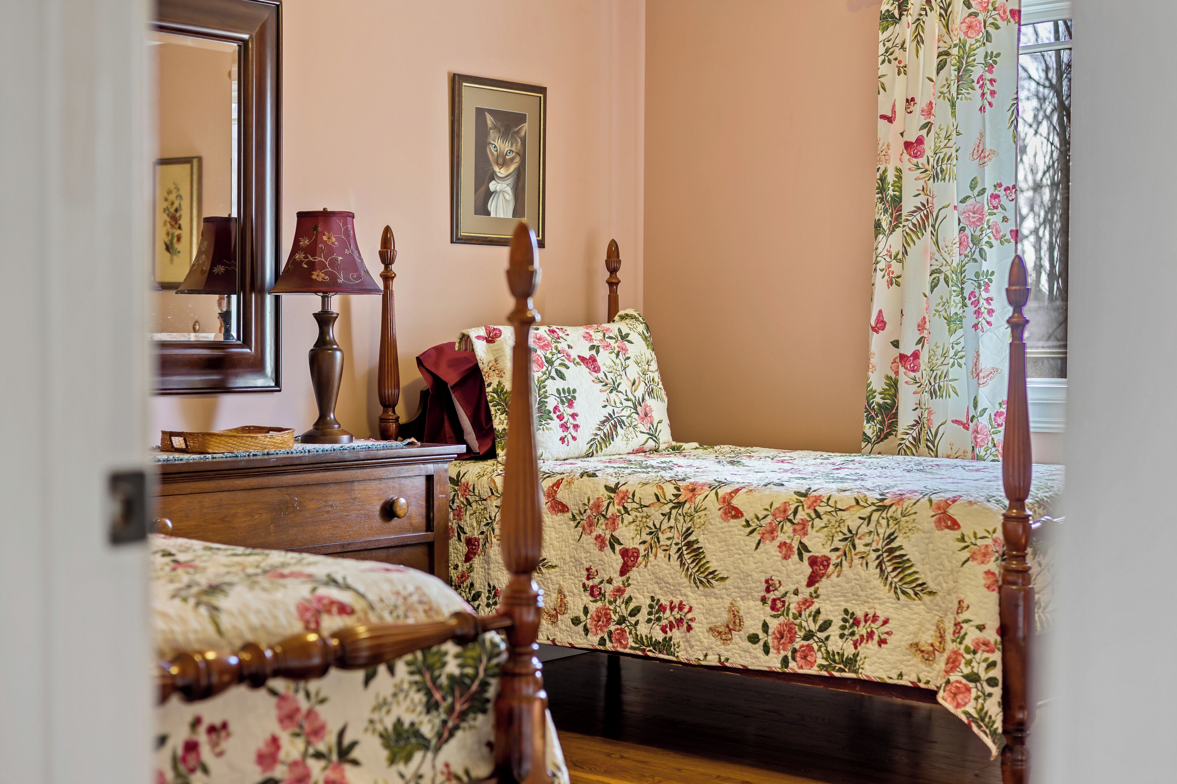 Une chambre à coucher avec un lit en bois, une table de chevet, une lampe, un miroir et un rideau à motifs floraux.