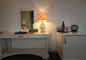 Un escritorio blanco con una lámpara, un espejo, un mueble pequeño y algunos objetos en la encimera.