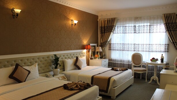 A hotel room with two beds, a desk, a chair, a lamp, and a window with curtains. - Nesta Boutique Hotel Hanoi (Hanoi)