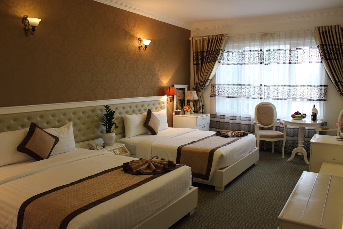 A hotel room with two beds, a desk, a chair, a lamp, and a window with curtains.