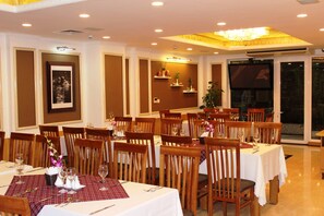 Un comedor con varias mesas, sillas y una pantalla de televisión.