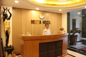 Una mesa de recepción con una recepcionista, una estatua y un cartel que dice 'NESTA HOTEL'.