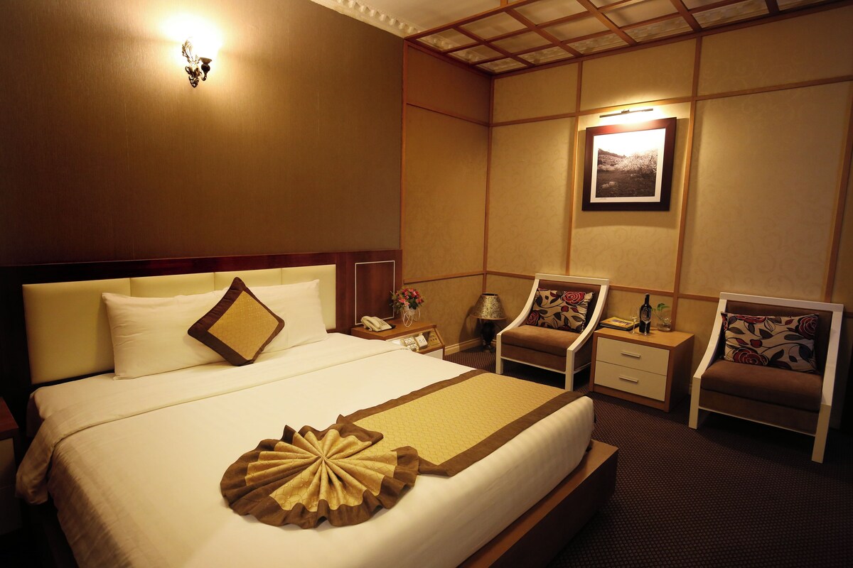 A hotel room with a large bed, two bedside tables, two chairs, a nightstand with a lamp, and a wall-mounted picture.
