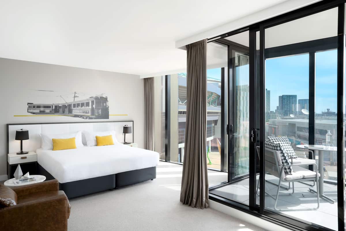 Een moderne hotelkamer met een groot bed, stadszicht, een balkon met zitgelegenheid en een raam met gordijnen.