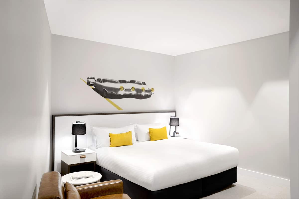 Een moderne hotelkamer met een groot bed, een nachtkastje met lamp, een kleine tafel en een bruine leren fauteuil.