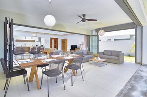 A modern open-plan living area with a dining table, chairs, sofas, and a ceiling fan. - Corail Bleu Private Pool & Garden Villas By LOV (Cap Malheureux)