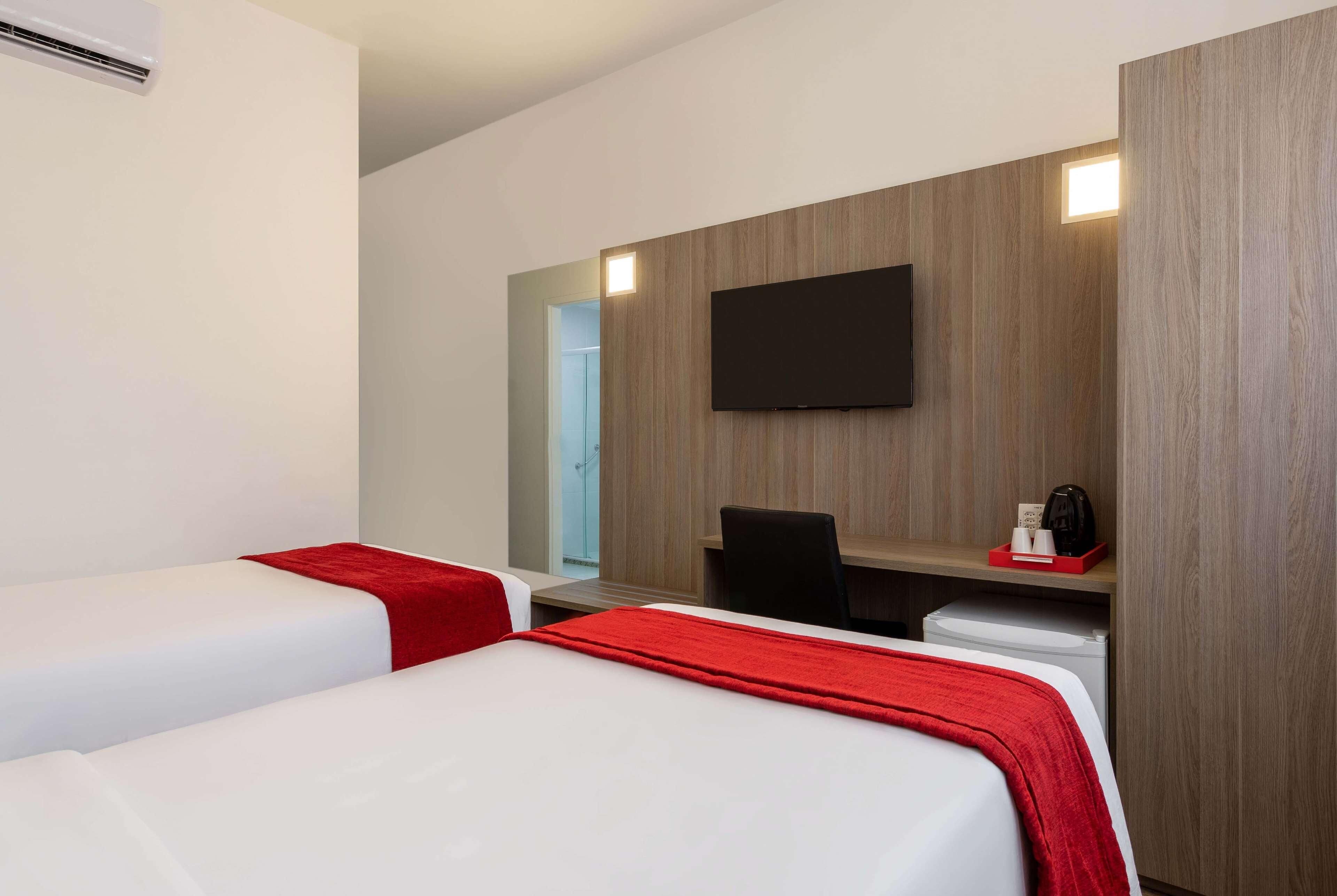 Quarto de hotel com duas camas, uma escrivaninha, uma cadeira, uma televisão de tela plana e uma cafeteira.