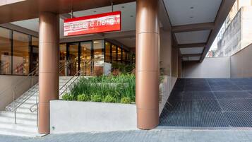 A hotel entrance with a red sign, large pillars, a staircase, and a small garden area.