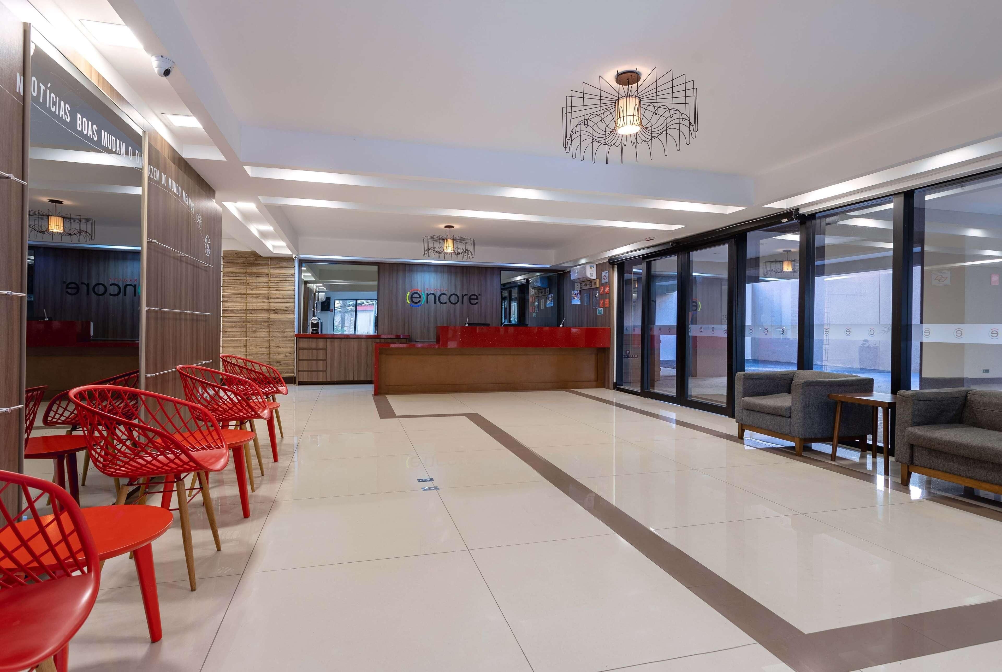 Um lobby moderno com balcão de recepção, cadeiras vermelhas e área de estar com sofás.