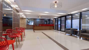 Um lobby moderno com balcão de recepção, cadeiras vermelhas e área de estar com sofás.