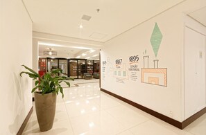 A hallway with a large potted plant, a wall with historical information, and a glass door leading to another area.