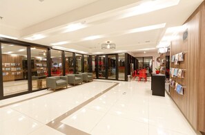 A hotel lobby with a reception desk, seating area, and a large glass wall.