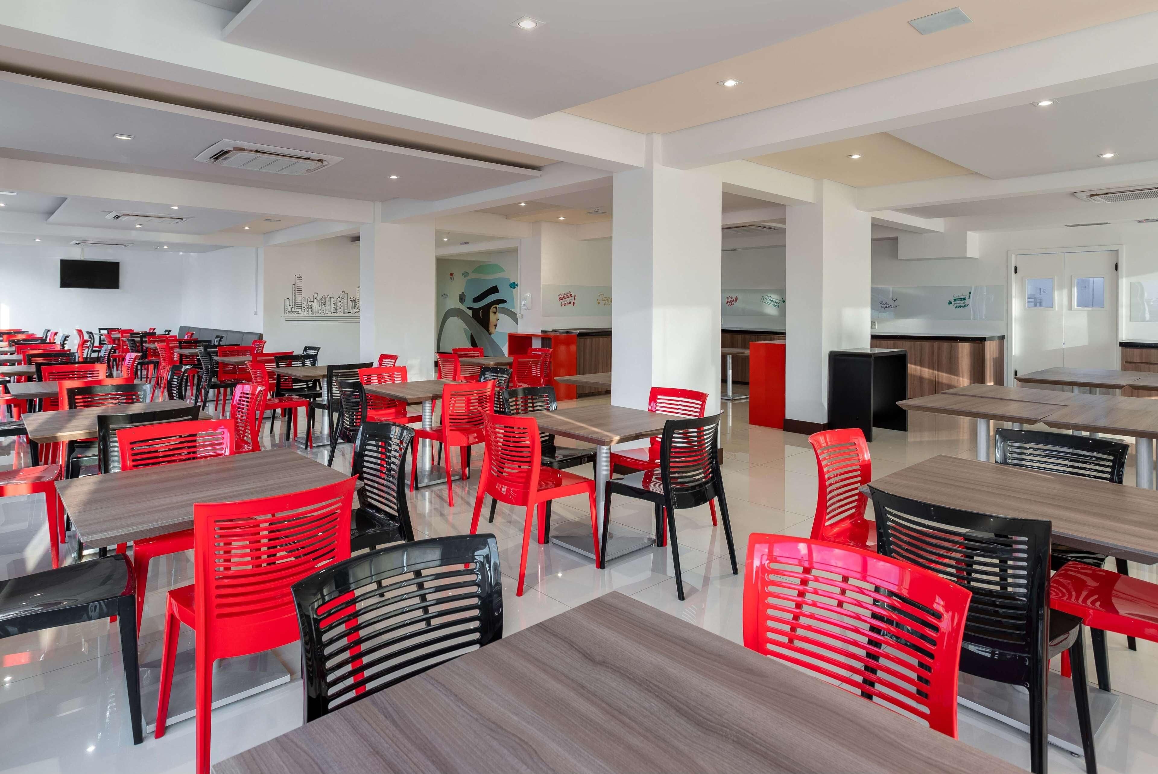 Uma sala de jantar ampla, com várias mesas e cadeiras, uma televisão de tela plana na parede e um design de interiores moderno.
