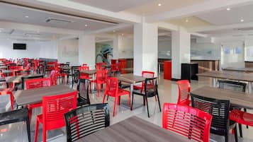 Uma sala de jantar ampla, com várias mesas e cadeiras, uma televisão de tela plana na parede e um design de interiores moderno.