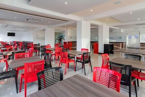 Uma sala de jantar ampla, com várias mesas e cadeiras, uma televisão de tela plana na parede e um design de interiores moderno.