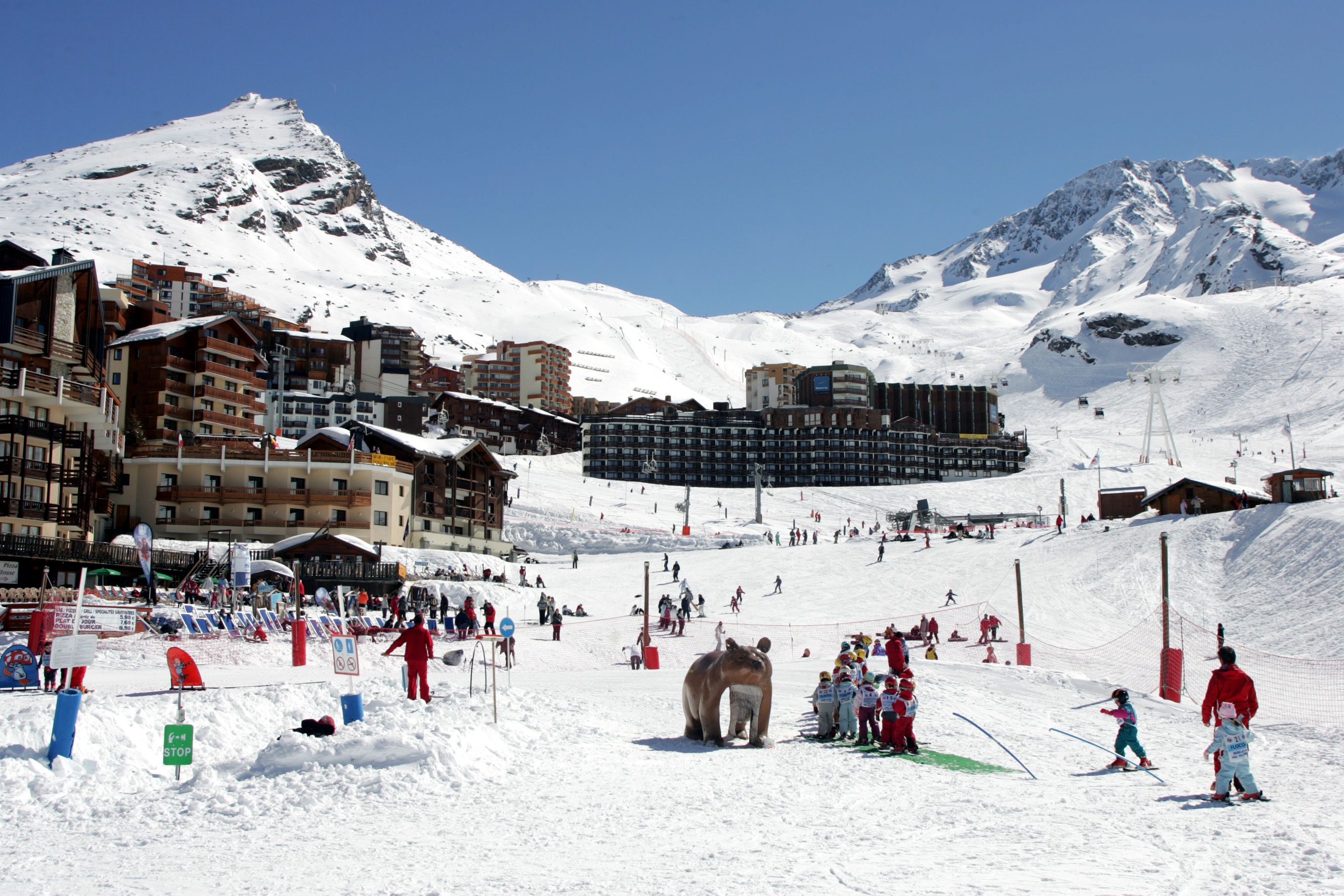 Une station de ski enneigée, avec des bâtiments, une piste de ski et une statue d’ours.