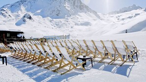 A snow-covered mountain landscape with a row of sun loungers and a building in the background. - Residence Odalys Tourotel (Les Belleville)
