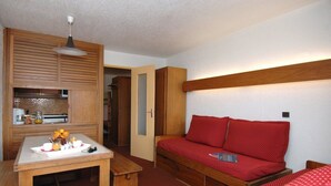 A compact room with a kitchenette, a wooden bed with red bedding, and a small dining table with breakfast items. - Residence Odalys Tourotel (Les Belleville)