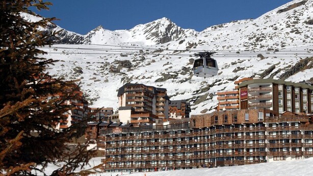 A ski resort with a cable car, a large building with multiple balconies, and snow-covered mountains in the background. - Residence Odalys Tourotel (Les Belleville)