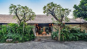 A courtyard with a thatched-roof structure, a stone wall, and a paved floor. - Radha Phala Resort and Spa (Ubud)