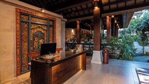 A reception area with a wooden reception desk, a television, and a decorative wall with intricate patterns. - Radha Phala Resort and Spa (Ubud)